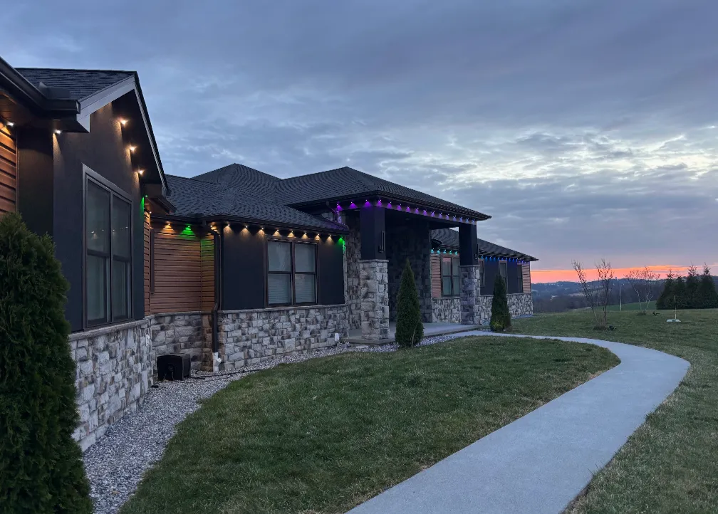 Modern farmhouse at sunset with green, purple, and warm white accent lighting along the rooflines